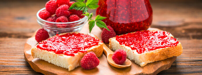 Weißbrot mit Himbeermarmelade auf Holzbrett, Himbeeren in Schale